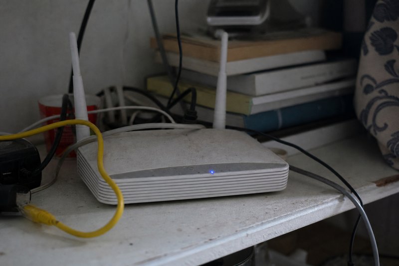 Router doméstico numa prateleira com cabos emaranhados e um pequeno LED azul aceso.